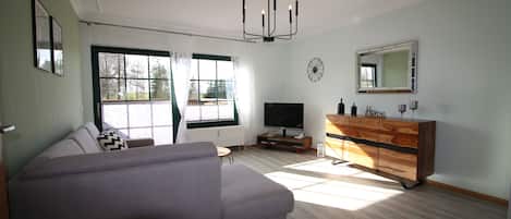 Uma sala de estar moderna com um sofá, uma televisão, um armário de madeira e uma janela grande.