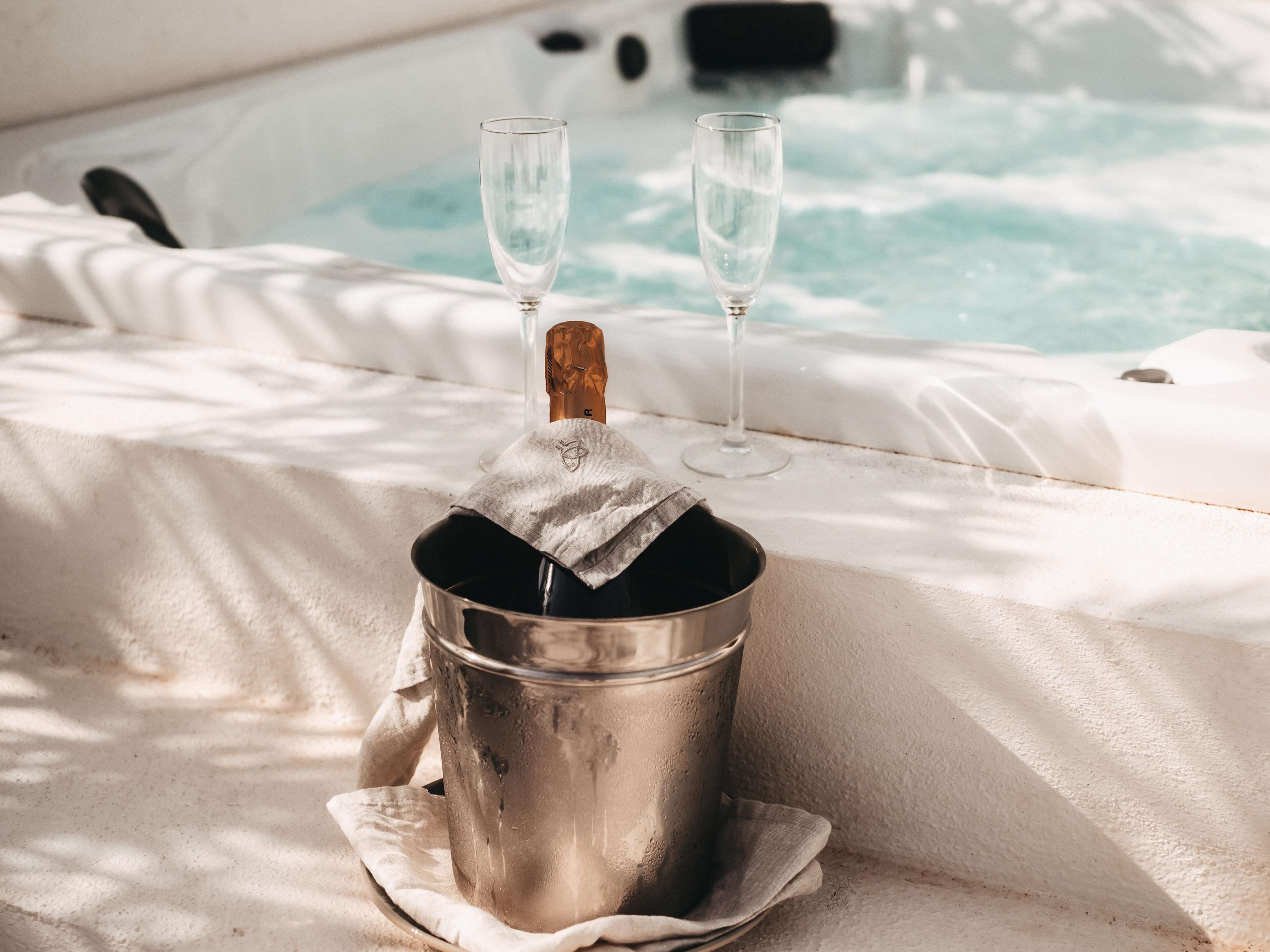 A hot tub with two champagne glasses and a bucket of champagne.