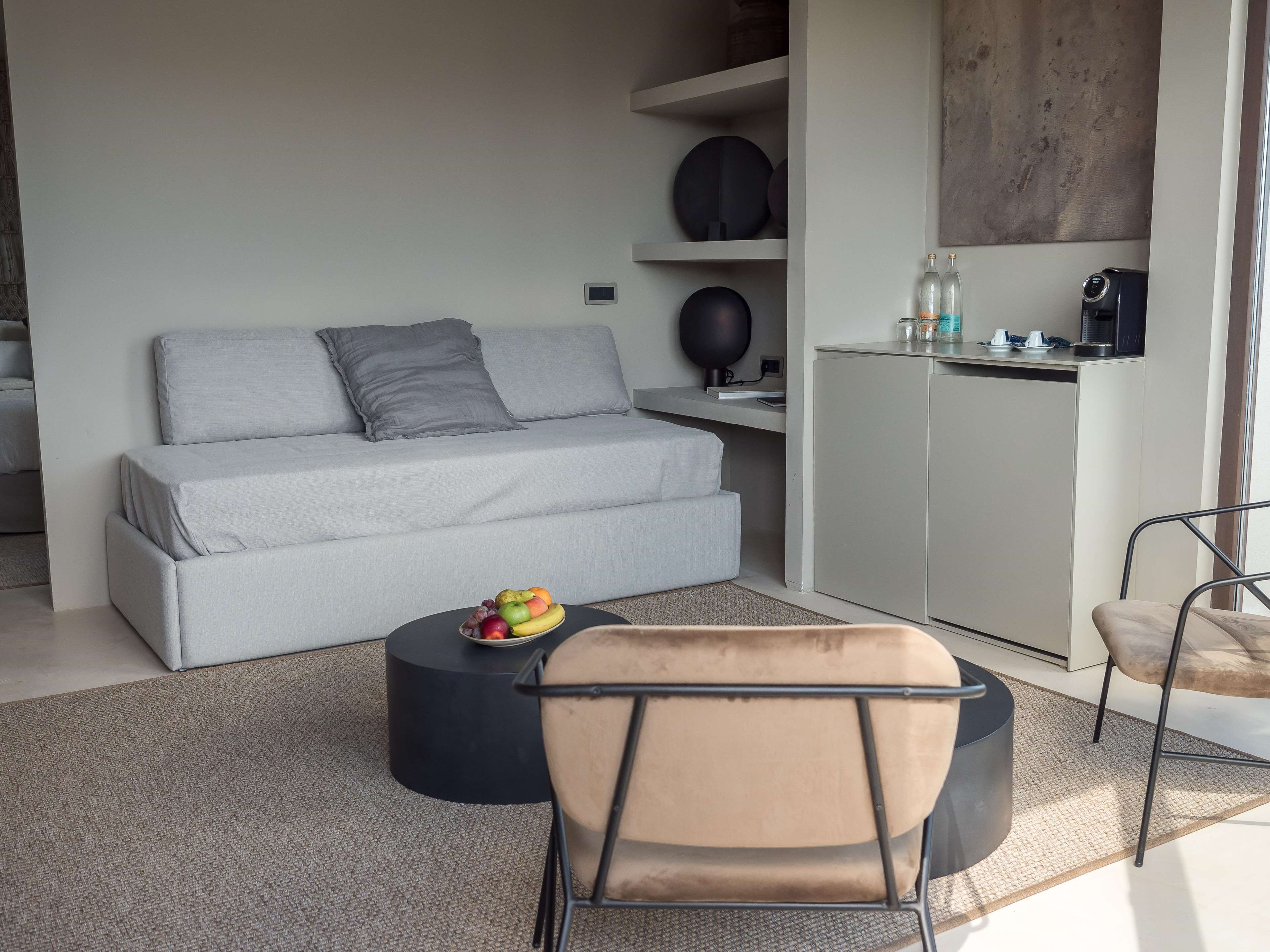 Ein modernes Wohnzimmer mit einem grauen Sofa, einem runden schwarzen Couchtisch und einem beigen Sessel.