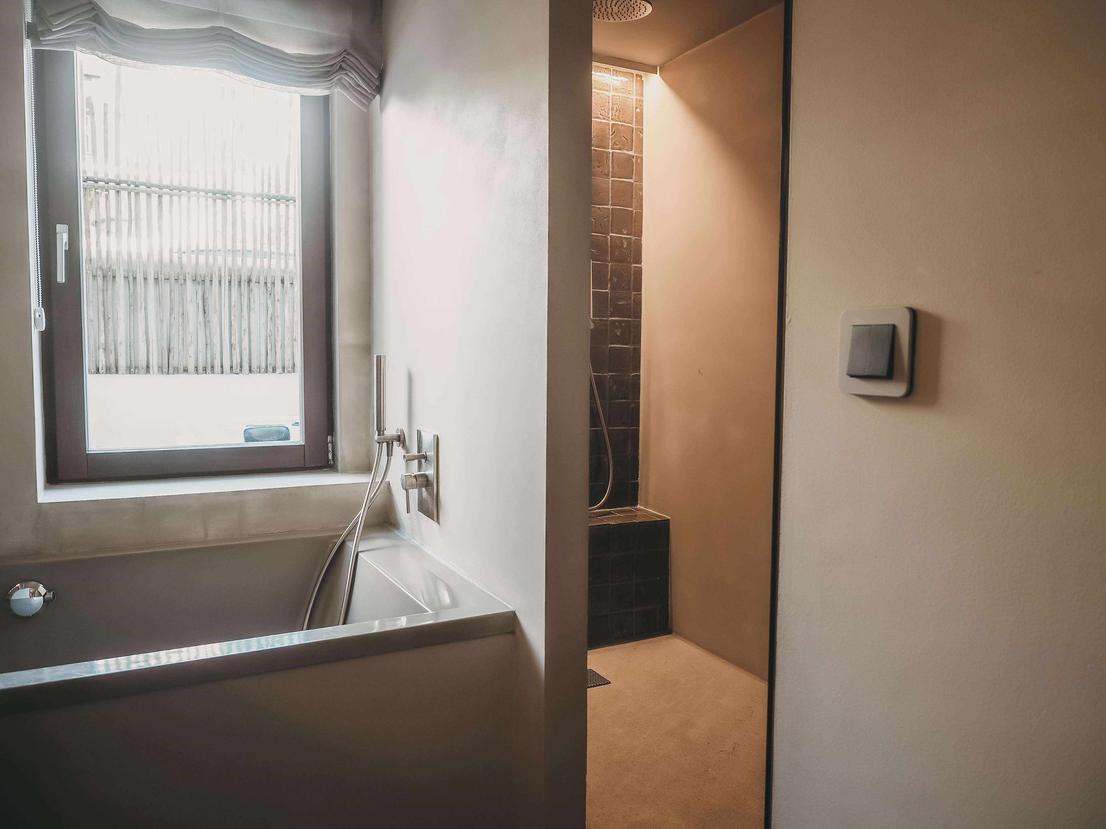 A bathroom with a bathtub, a shower, and a window with a curtain.