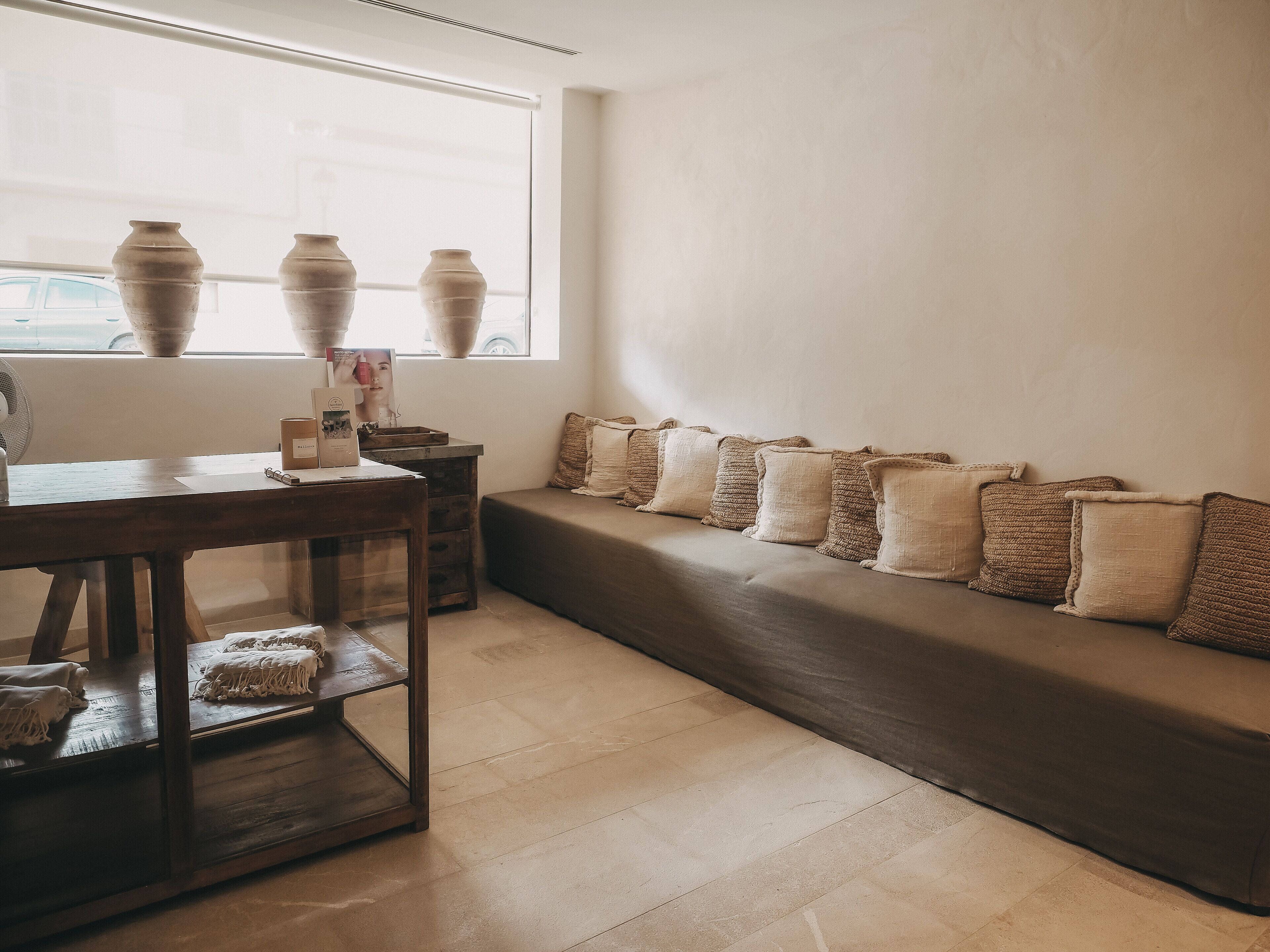 Una habitación con una mesa de madera, un banco con cojines tejidos y una ventana con jarrones.