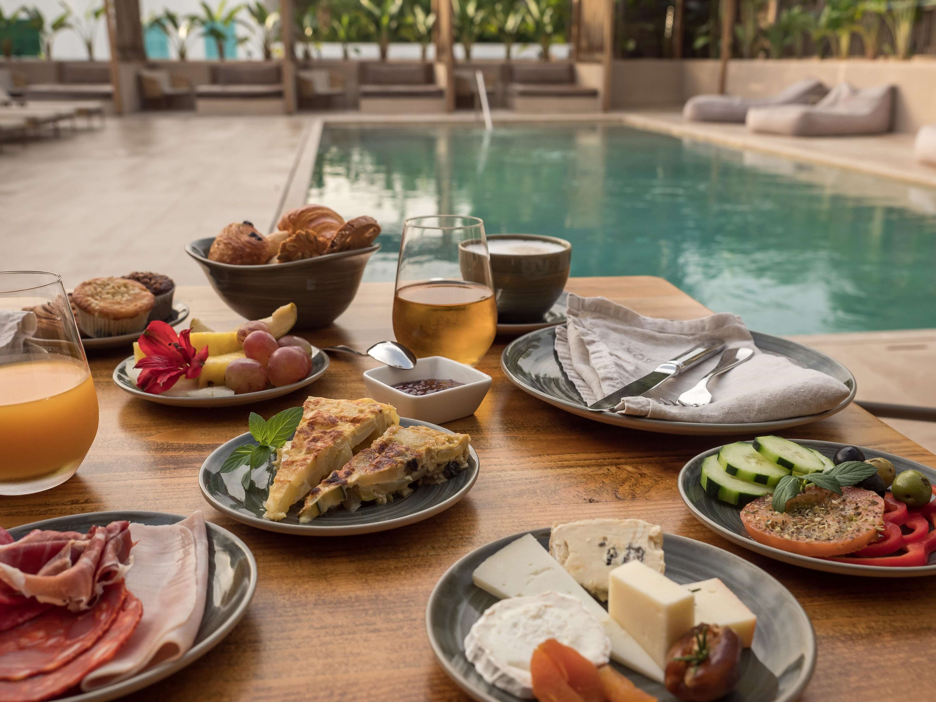 Un buffet de petit-déjeuner proposant une variété d’aliments, un verre de jus de fruits et une piscine en arrière-plan.