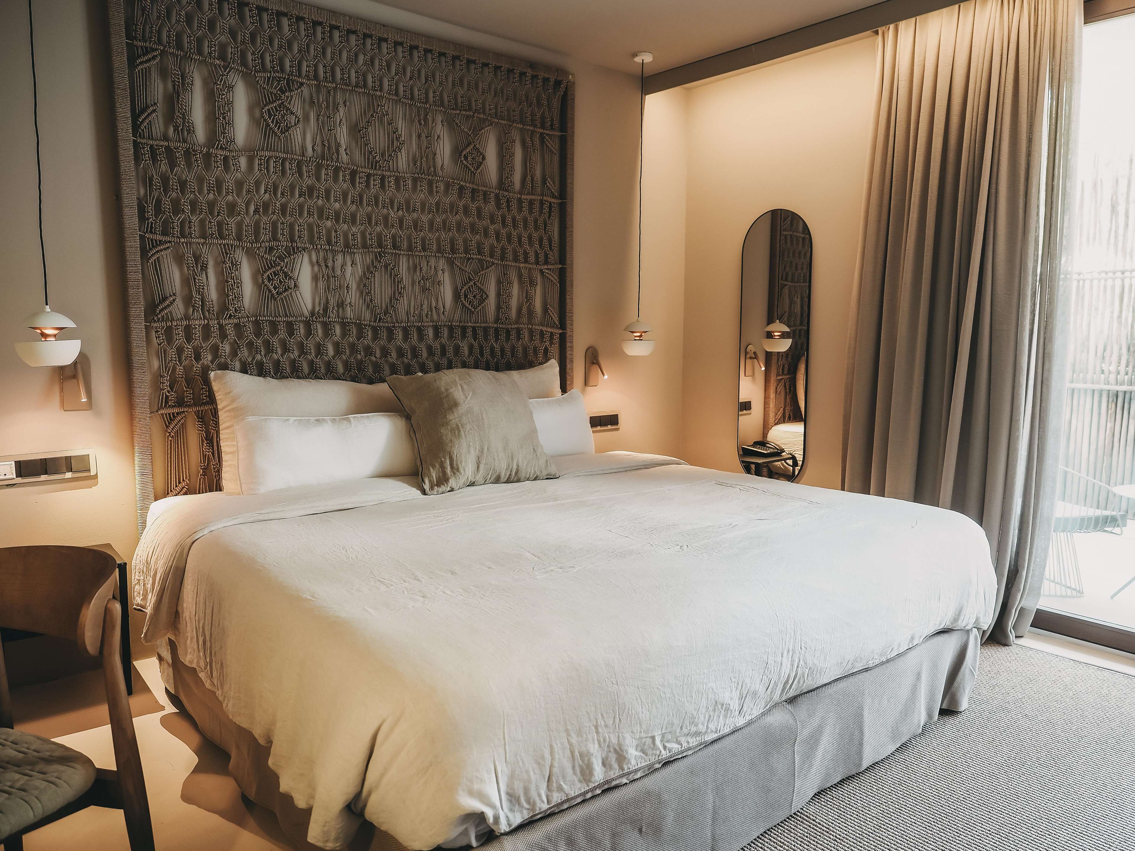 Habitación de hotel moderna con una cama grande, un cabecero de macramé, un espejo amplio y vistas al exterior.