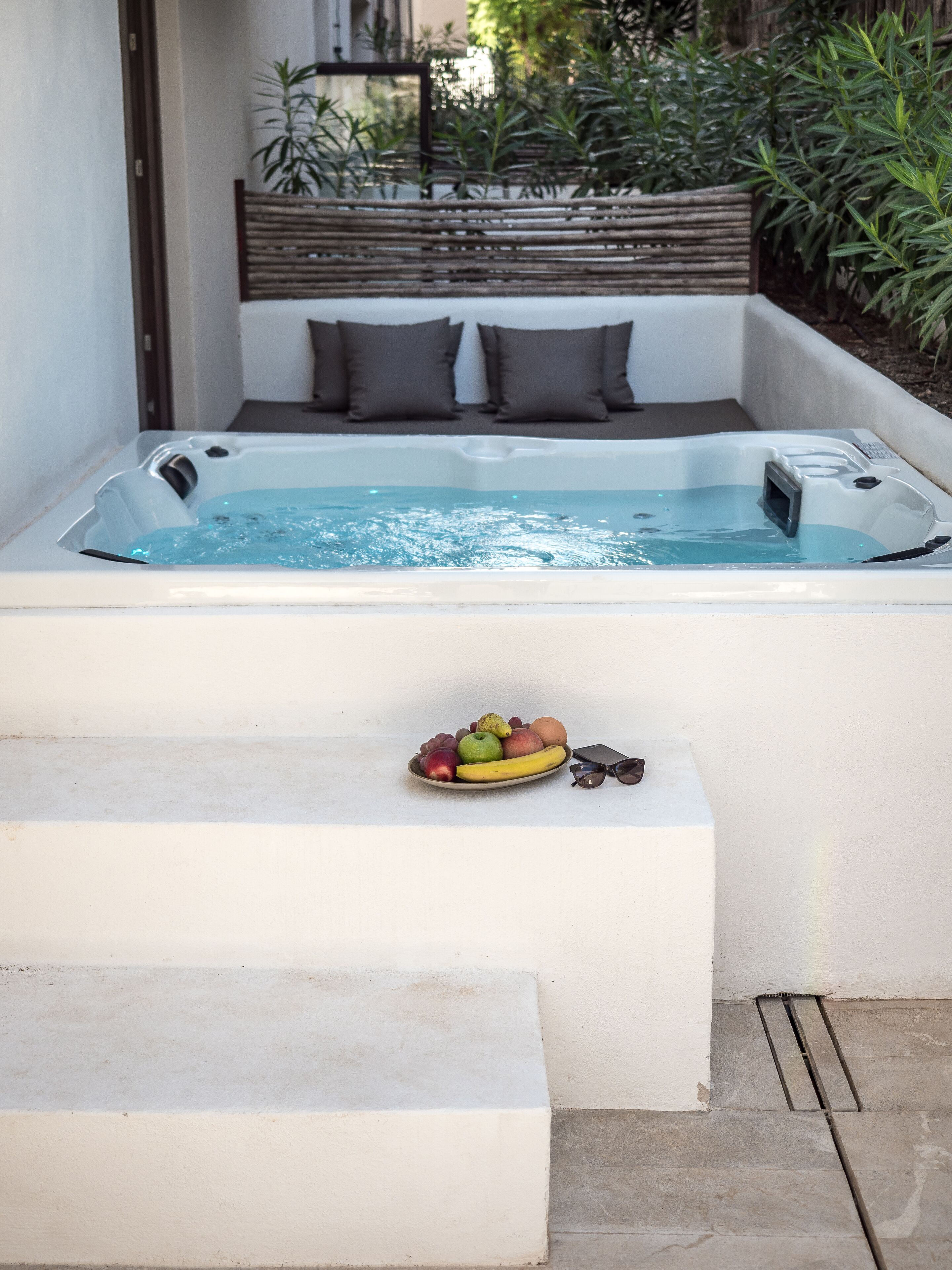 Ein Whirlpool mit einem hölzernen Kopfteil und einer Schale mit Früchten auf einer Ablage.