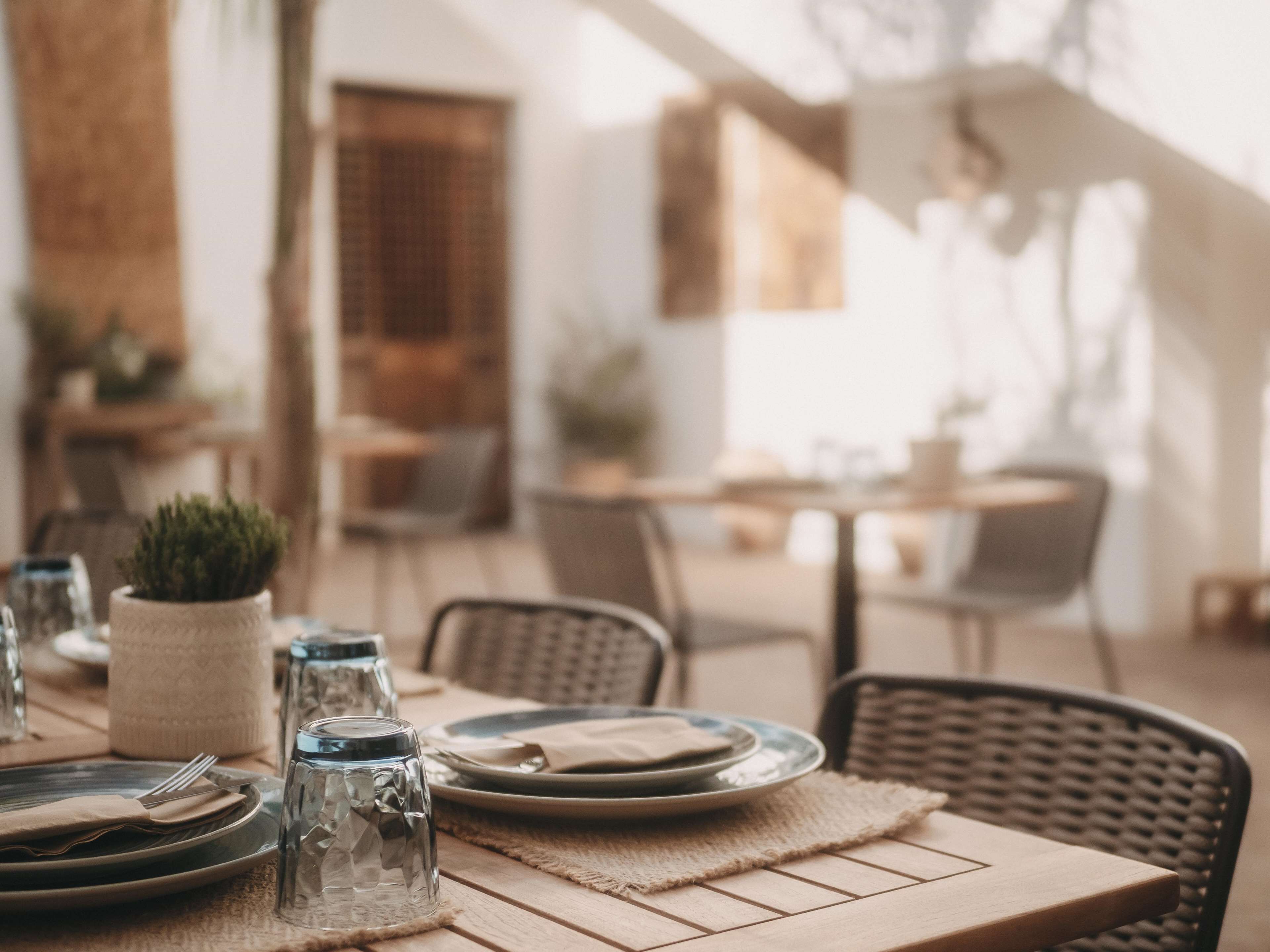 Una mesa de comedor dispuesta con platos, cubiertos y cristalería, con un mantel tejido y una pequeña planta en maceta.