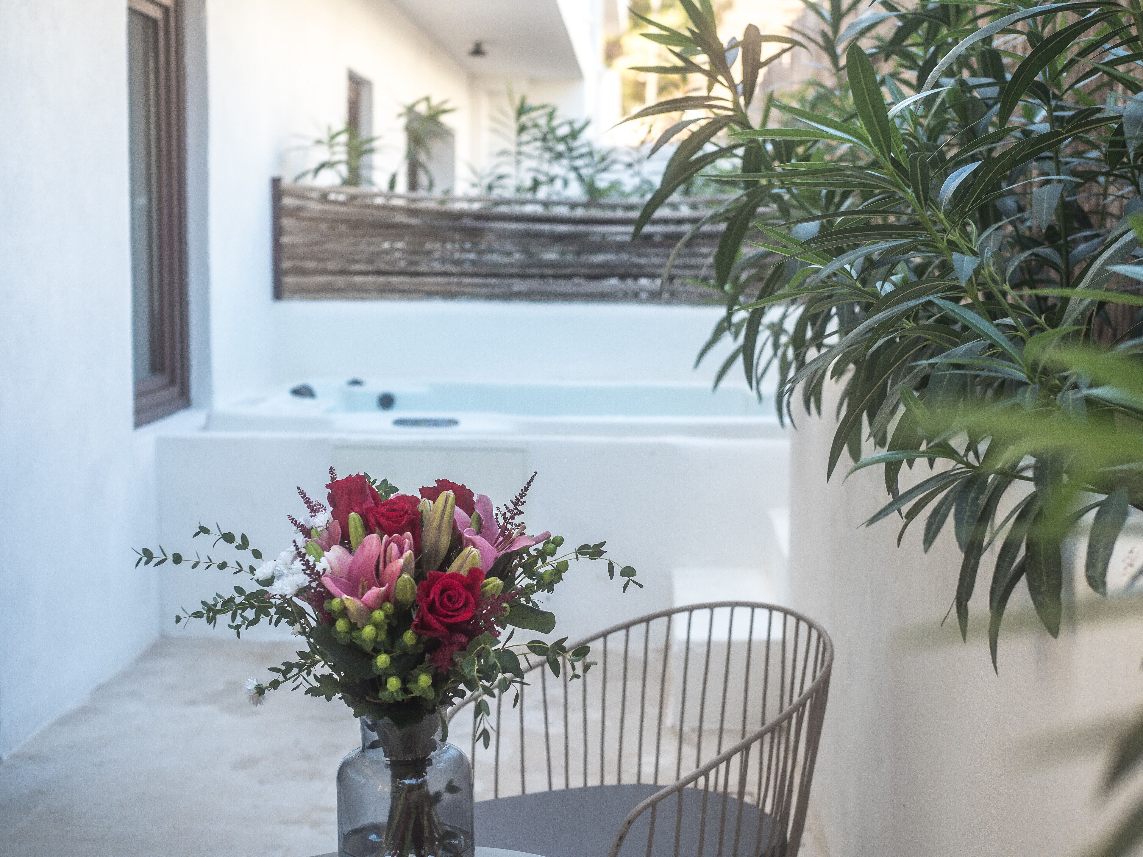 Una stanza con una vasca da bagno bianca, una sedia in metallo e un vaso di fiori.