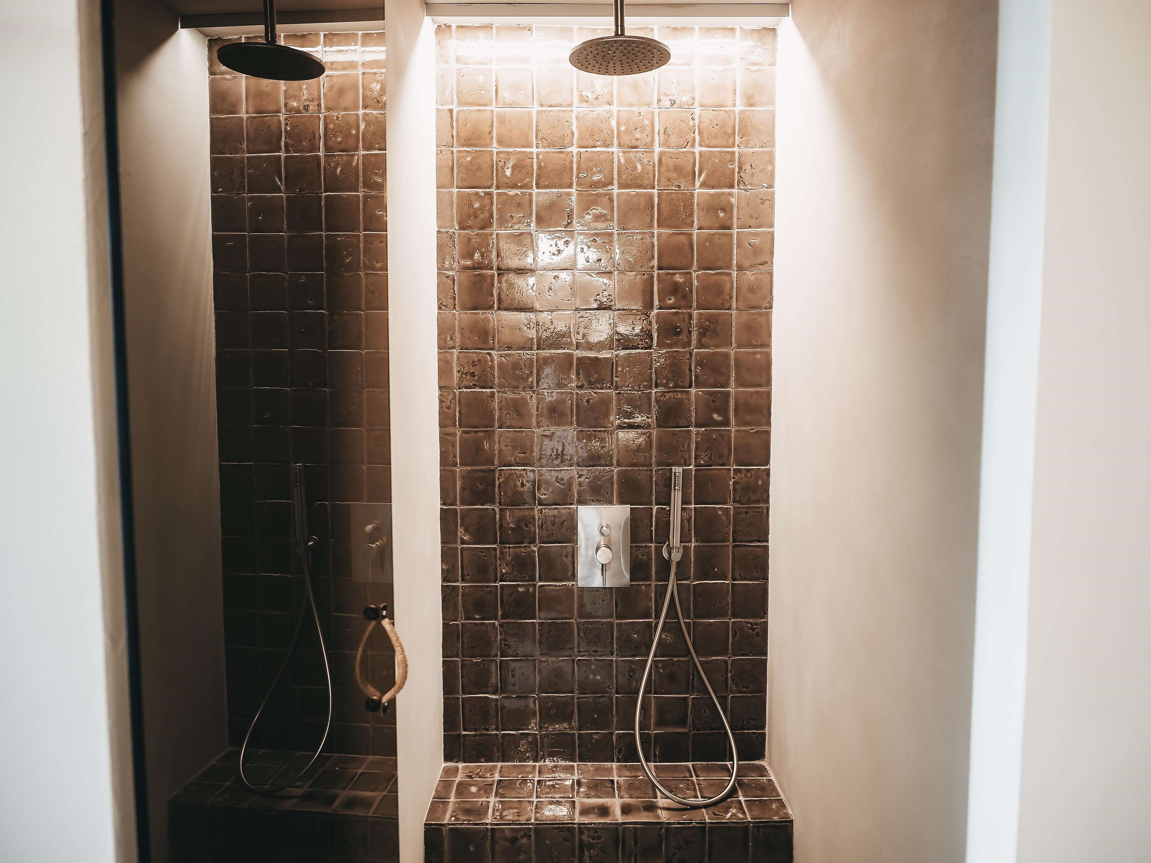 A shower with a tiled wall, a handheld showerhead, and a wall-mounted faucet.