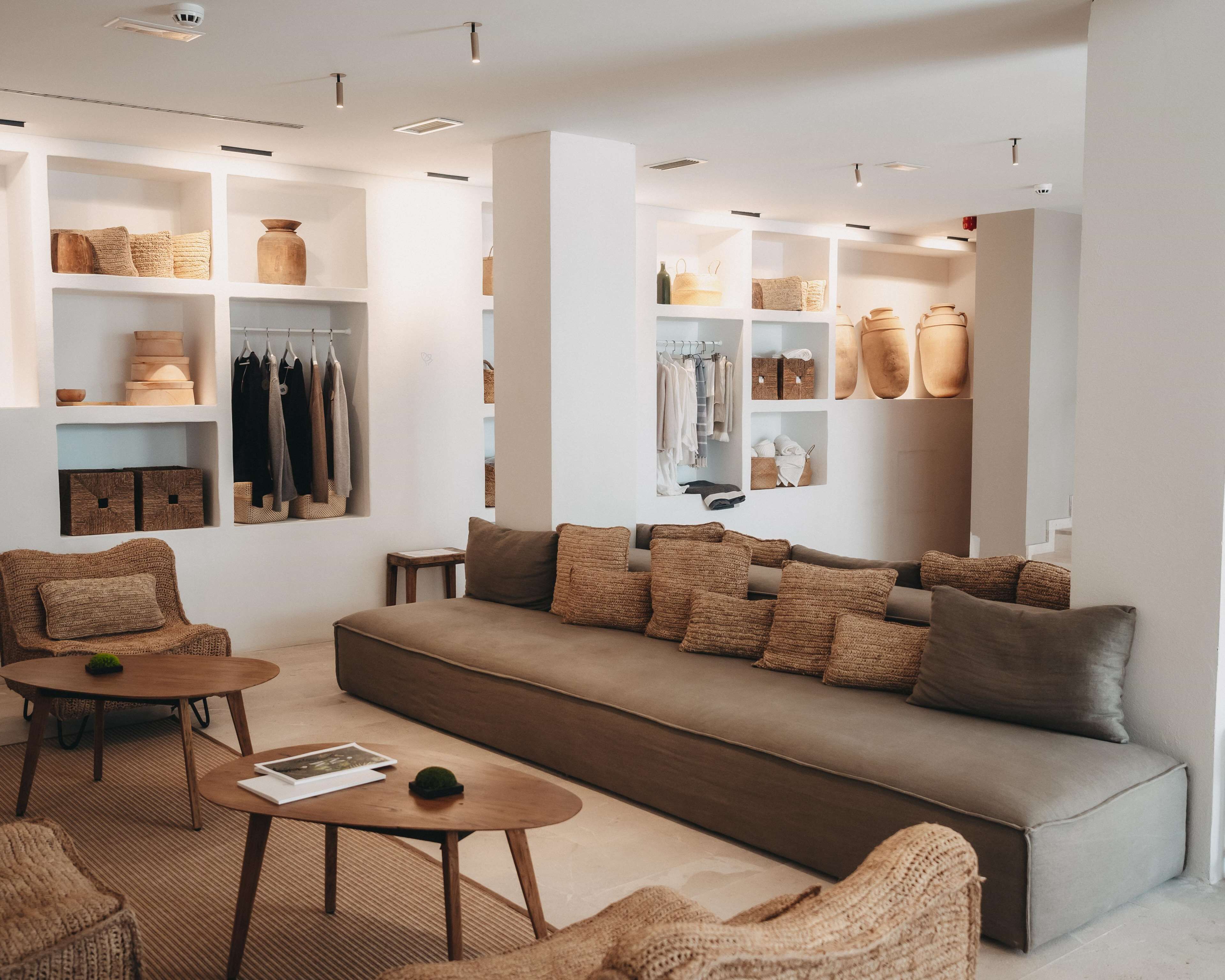 Una sala de estar moderna con un sofá, dos sillones y una mesa de centro. Hay estanterías con cajas de almacenamiento y ropa.