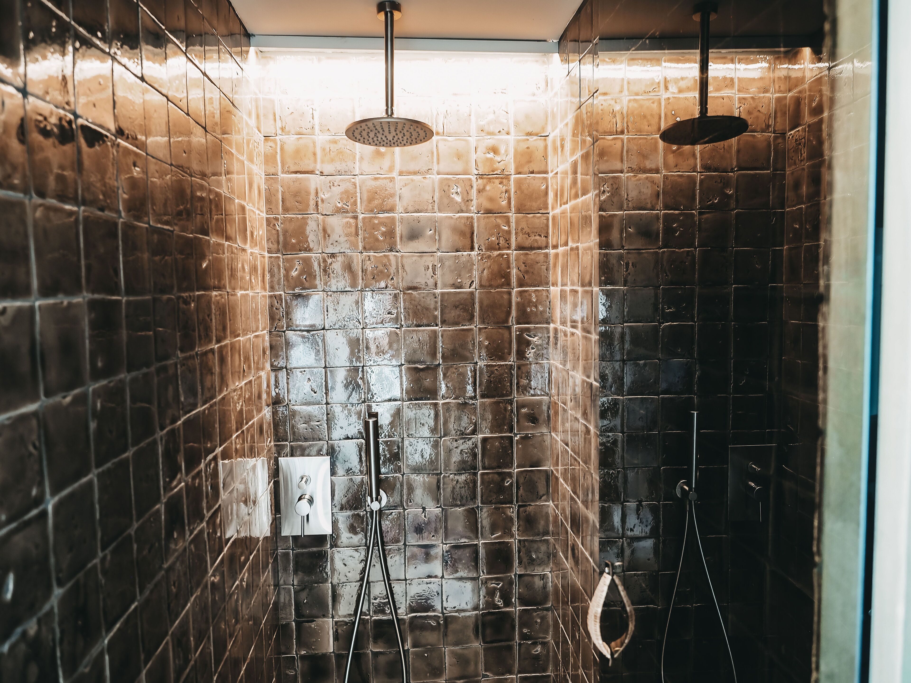 Douche met een regenkop en een handdouche, betegelde wanden en een zichtbaar bedieningspaneel.