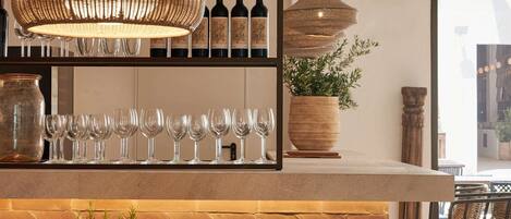 Un espace bar agrémenté d’un mur en bois disposé en motif chevron, d’une table ronde en bois avec des chaises, et d’un luminaire suspendu en osier.