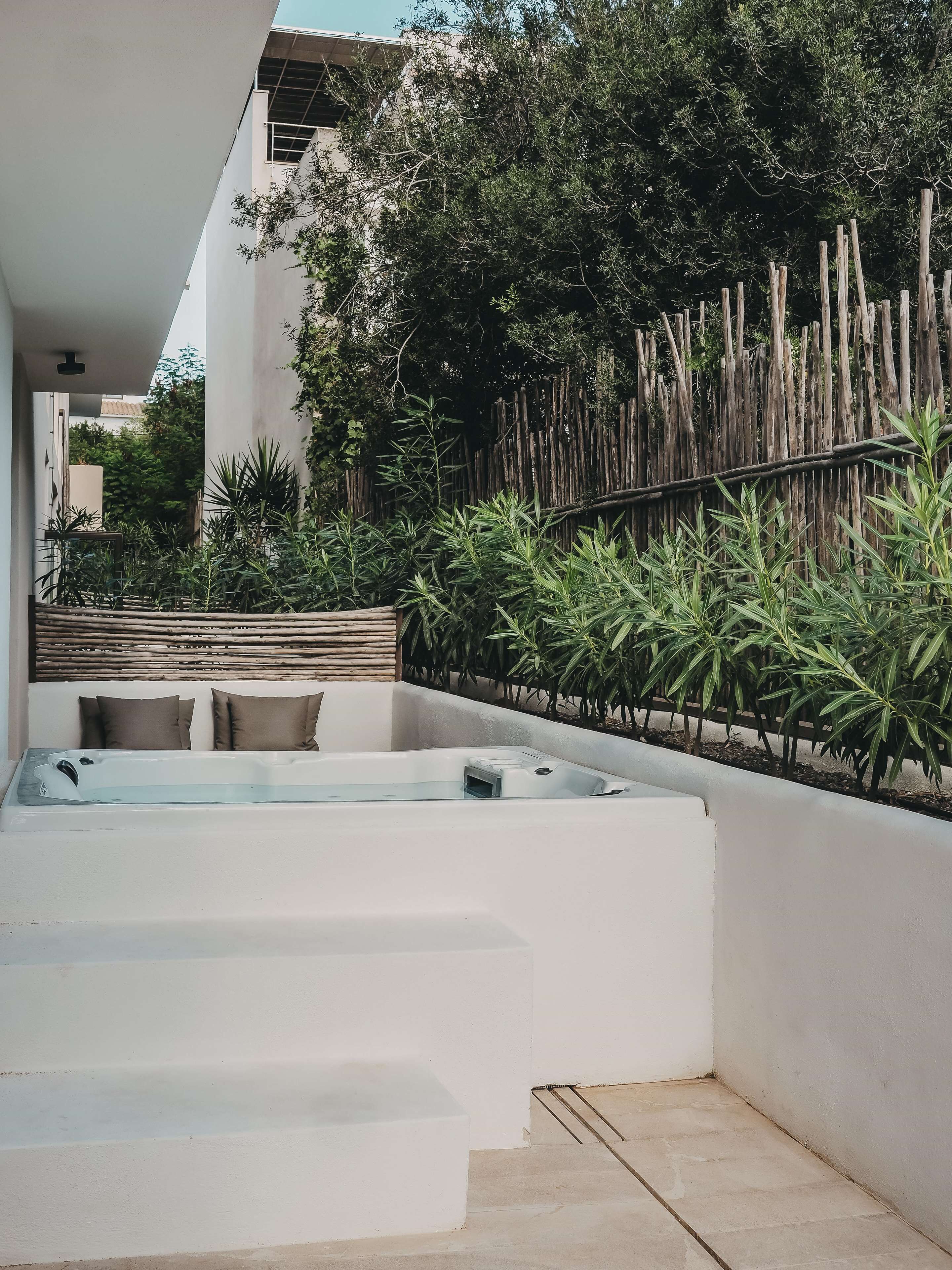Een wellnessruimte met een jacuzzi, een houten hek en weelderige begroeiing.