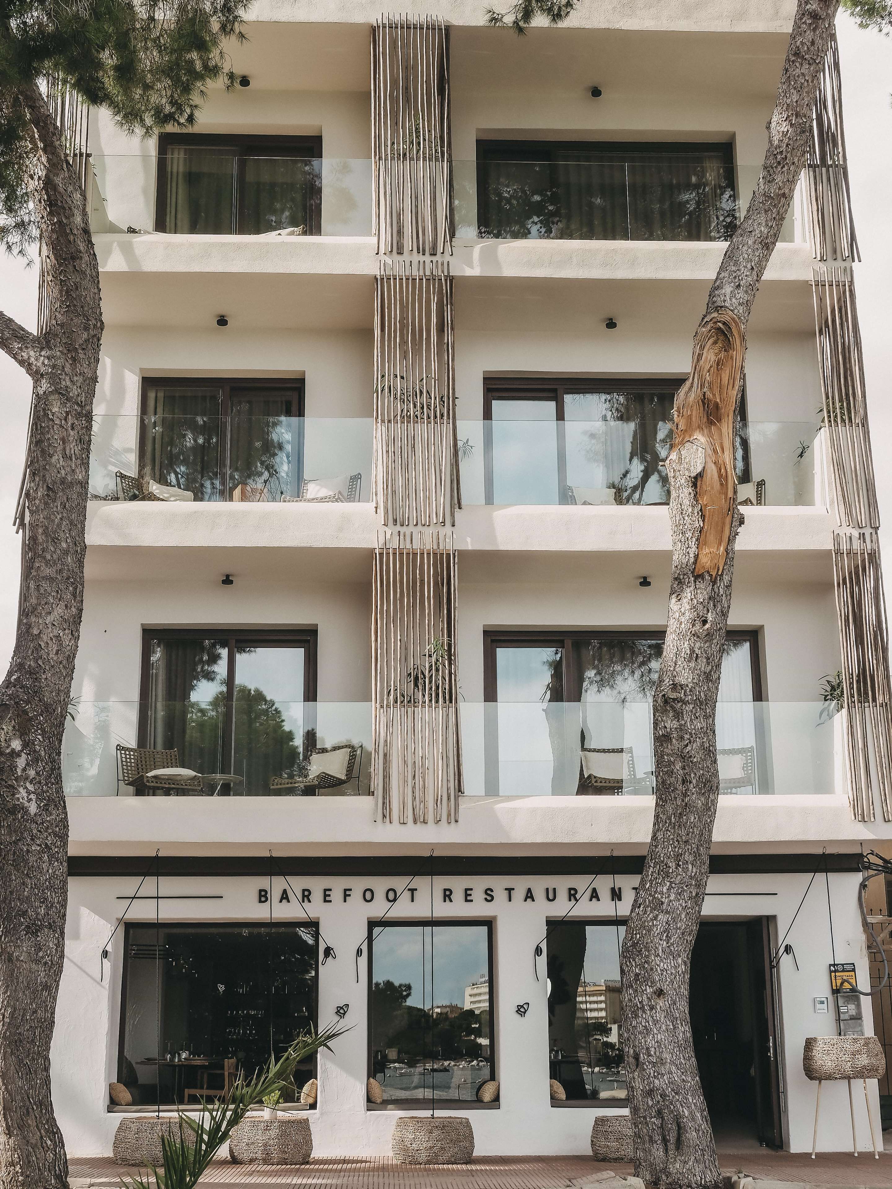 A multi-story building with a modern architectural design, featuring balconies with glass railings and a sign for "Barefoot Restaurant" at the ground level.