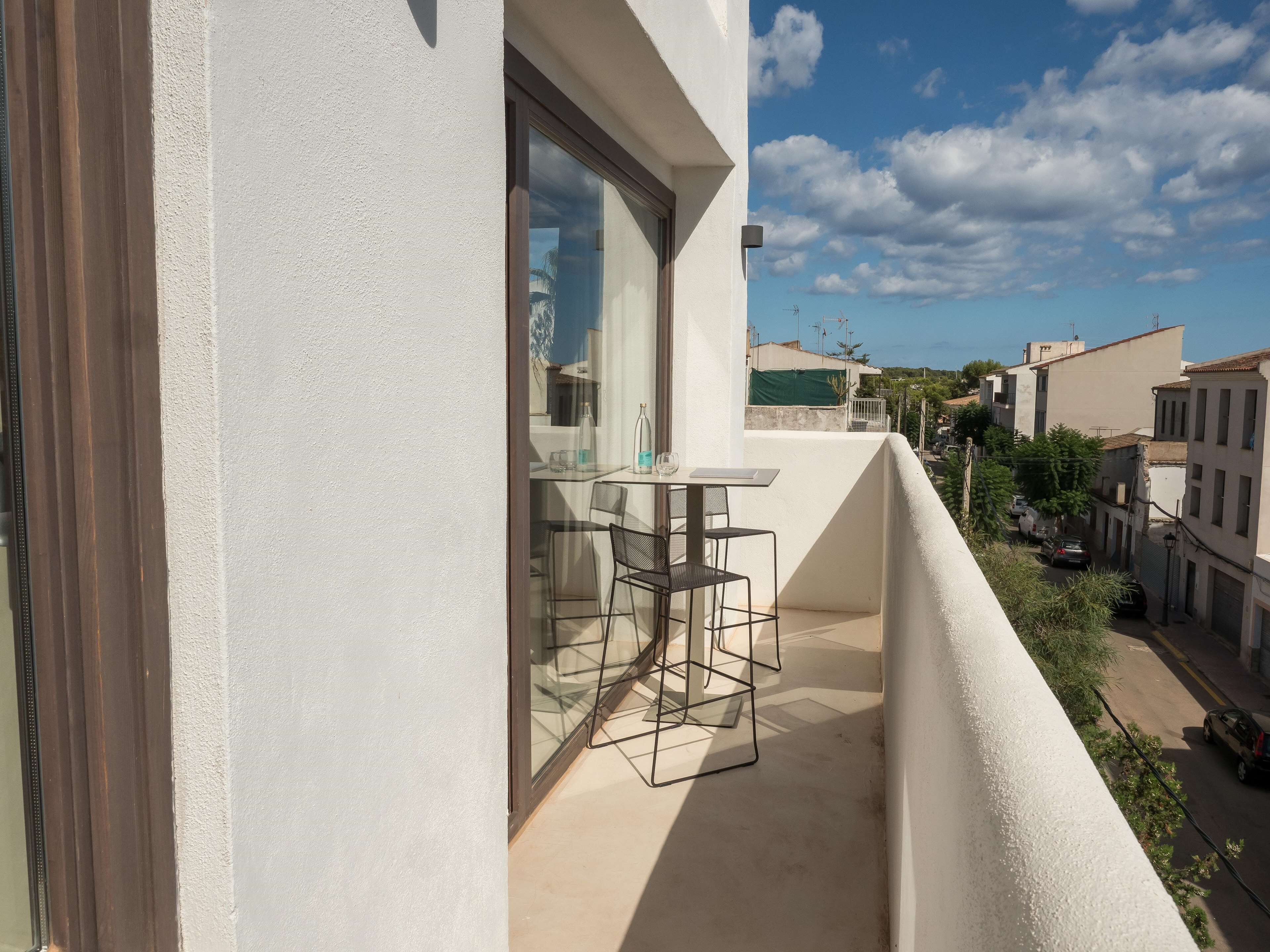 Ein Balkon mit Tisch und Stühlen, mit Blick auf eine Straße mit Gebäuden und parkenden Autos.