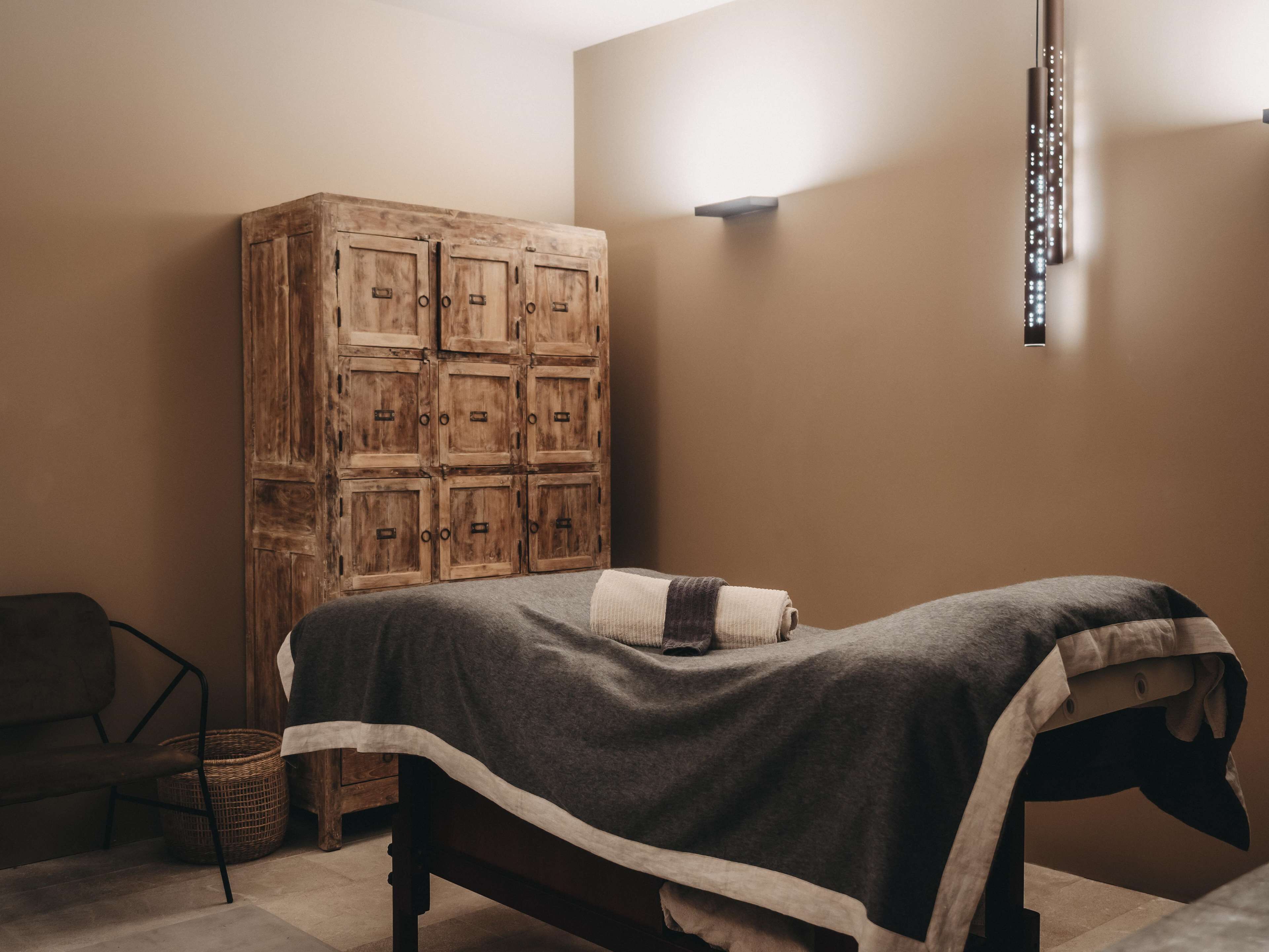 Ein Zimmer mit einem Bett, einem Holzschrank, einem Korbwannenkorb und einer Wandleuchte.
