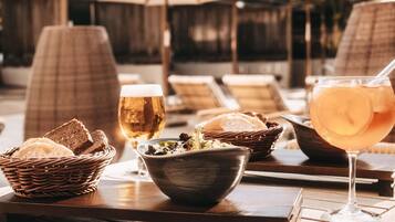 Una mesa con una jarra de cerveza, un vaso de bebida helada, un bol de ensalada y un cesto de pan.