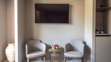 A modern living room with two armchairs, a flat-screen TV, a wicker side table with fruit, and a large vase.