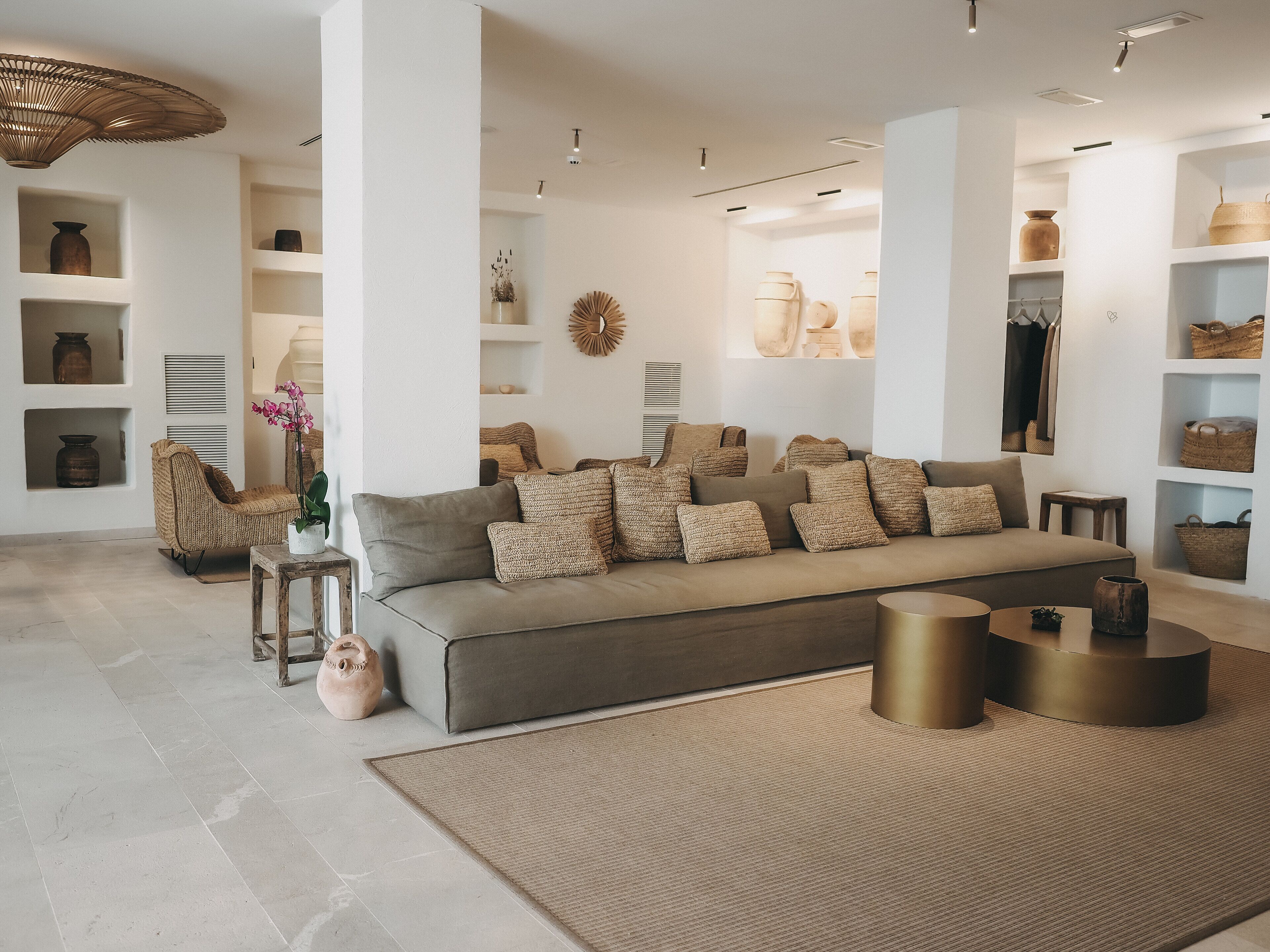 Un salon moderne avec un canapé gris, de nombreux coussins, un tapis tissé et divers objets décoratifs disposés sur des étagères et des tables.