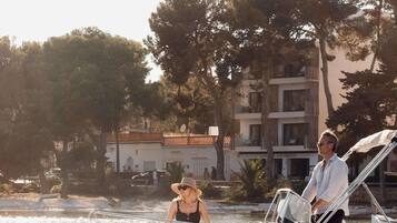 Un bote con dos personas navegando en un cuerpo de agua, con edificios y árboles al fondo.