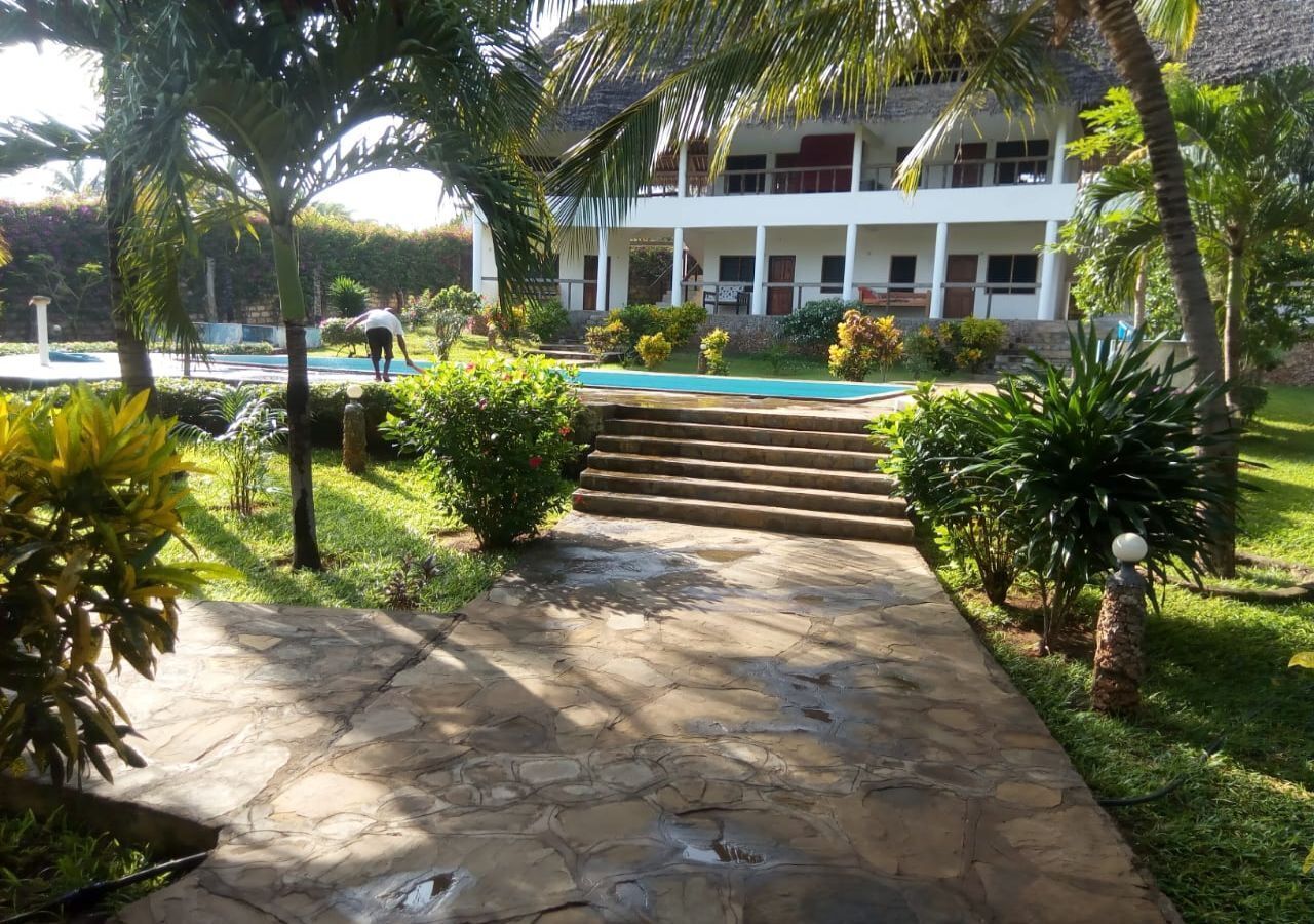 A stone pathway leading to a pool area with a two-story building in the background.