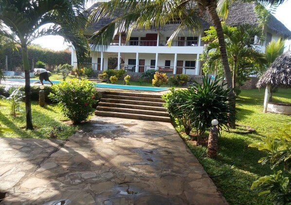 A stone pathway leading to a building with a pool, surrounded by lush greenery and palm trees. - Bonora Villa Malindi (Malindi)