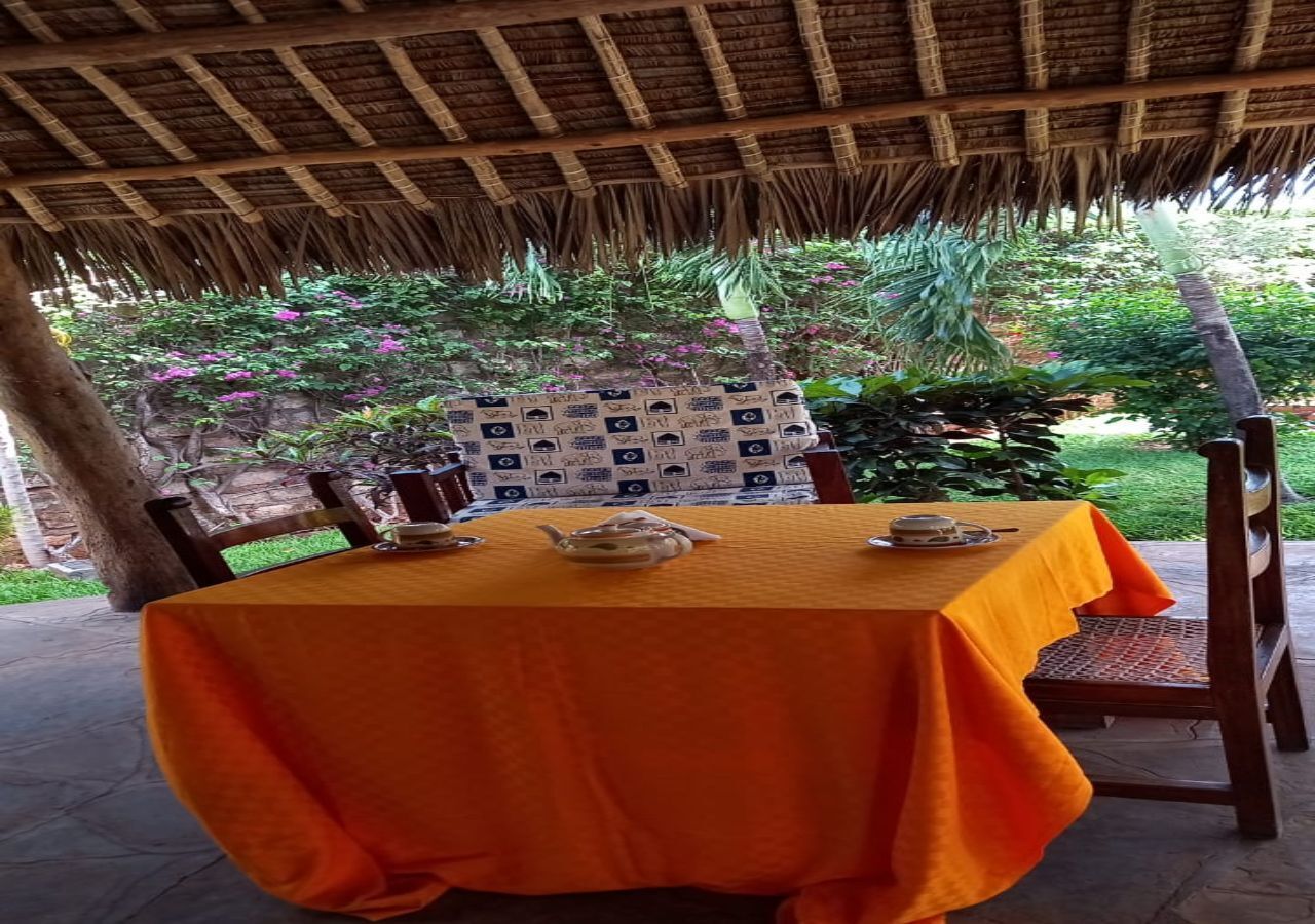 Una mesa con mantel naranja, sillas de madera y una pared con diseño al fondo.