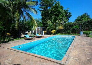 A rectangular swimming pool with clear blue water, surrounded by stone tiles. There are lounge chairs and a small building in the background. - Bonora Villa Malindi (Malindi)