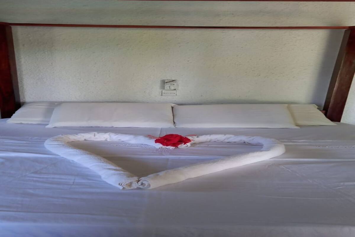 Una cama con ropa blanca y una disposición de toallas en forma de corazón, con una rosa roja.