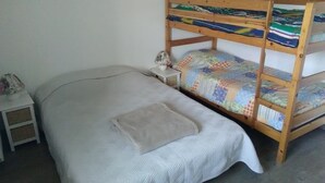 A bunk bed with a white mattress and a quilted blanket, a bedside table with a lamp, and a small nightstand with a basket. - Ecological country house (Èvres)