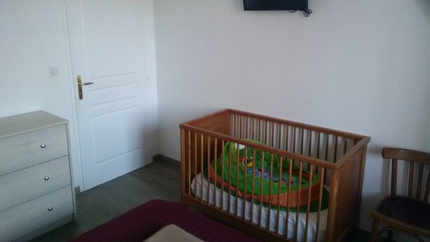 A room with a white door, a small wooden crib with a green mattress, a wooden chair, and a flat-screen TV on the wall. - Ecological country house (Èvres)