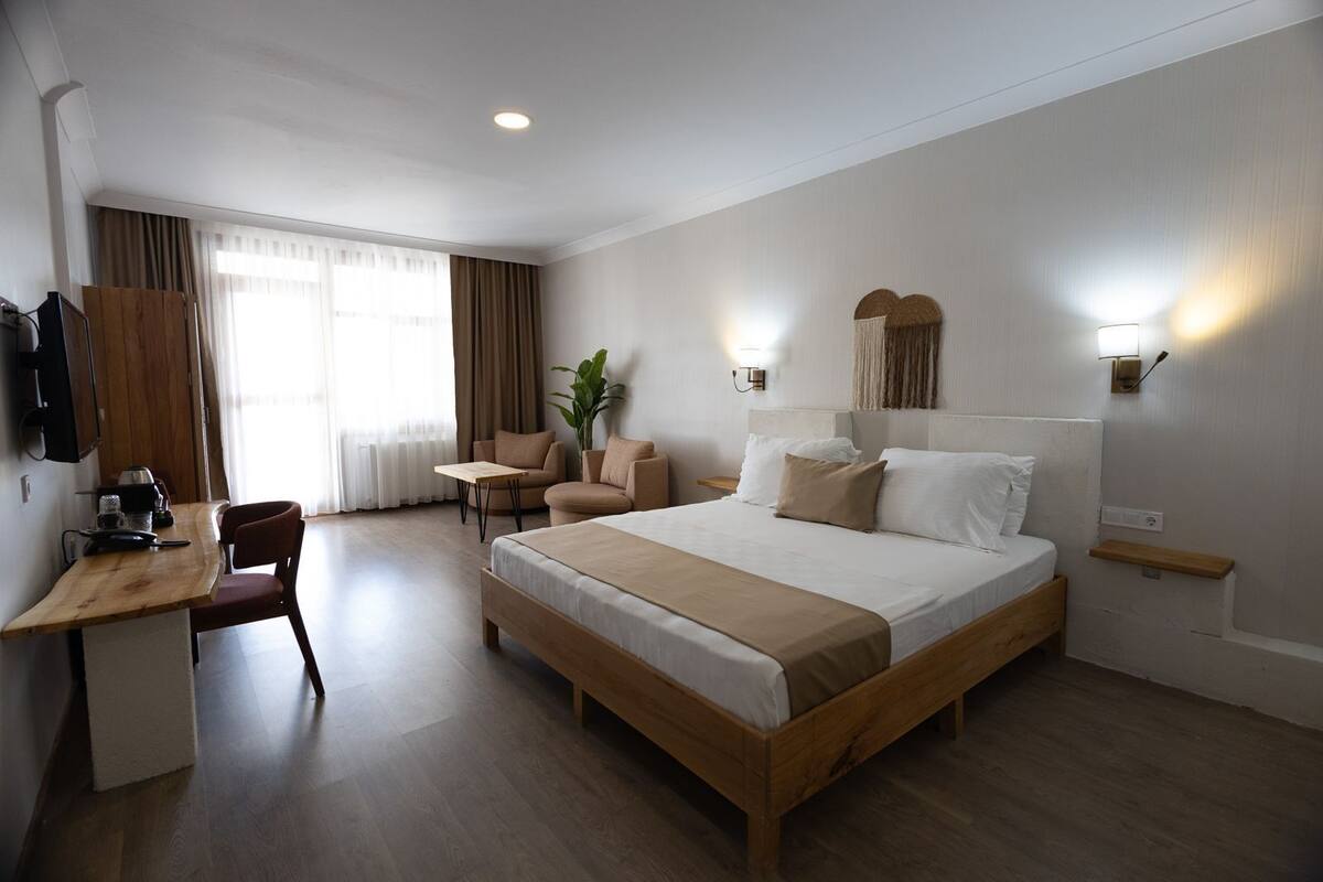 A hotel room with a large bed, a desk with a chair, a small table, and a TV.