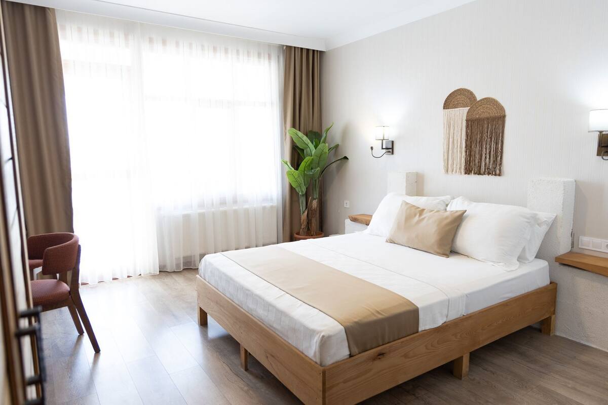 A hotel room with a wooden bed, a desk, a chair, and a large window with curtains.