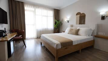 Habitació d'hotel amb un llit de fusta, una taula de treball amb una cadira, televisió i una finestra gran amb cortines.