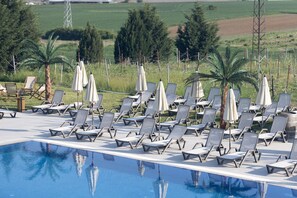 A poolside area with sun loungers and umbrellas, surrounded by greenery and a clear sky. - The Rest Port Village Hotel (Havsa)