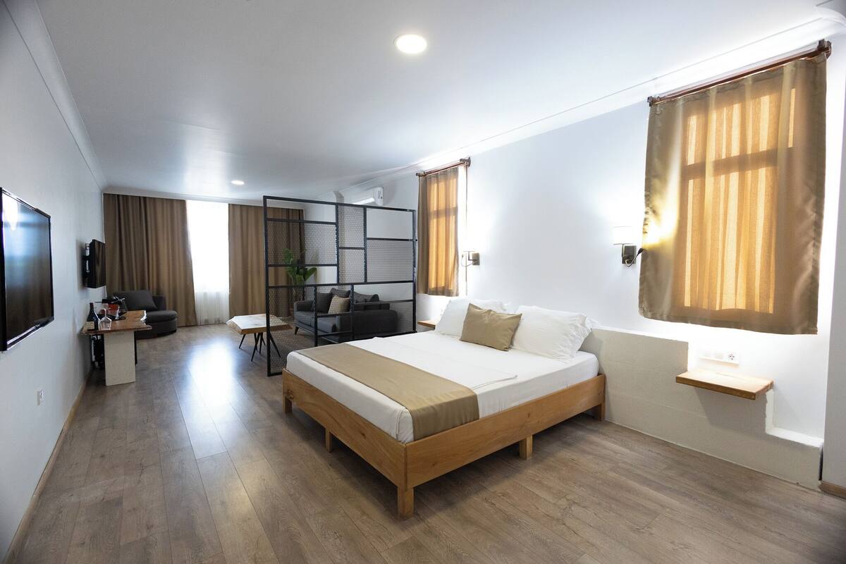 A modern hotel room with a wooden bed, a desk, a chair, and a TV.