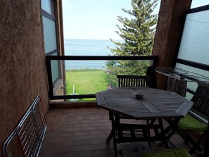 A balcony with a table and chairs, overlooking a grassy area and the sea. - Studio les pieds dans, santa lucia (Santa-Lucia-di-Moriani)