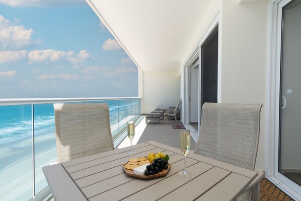 A balcony with a table set for a meal, overlooking the ocean.