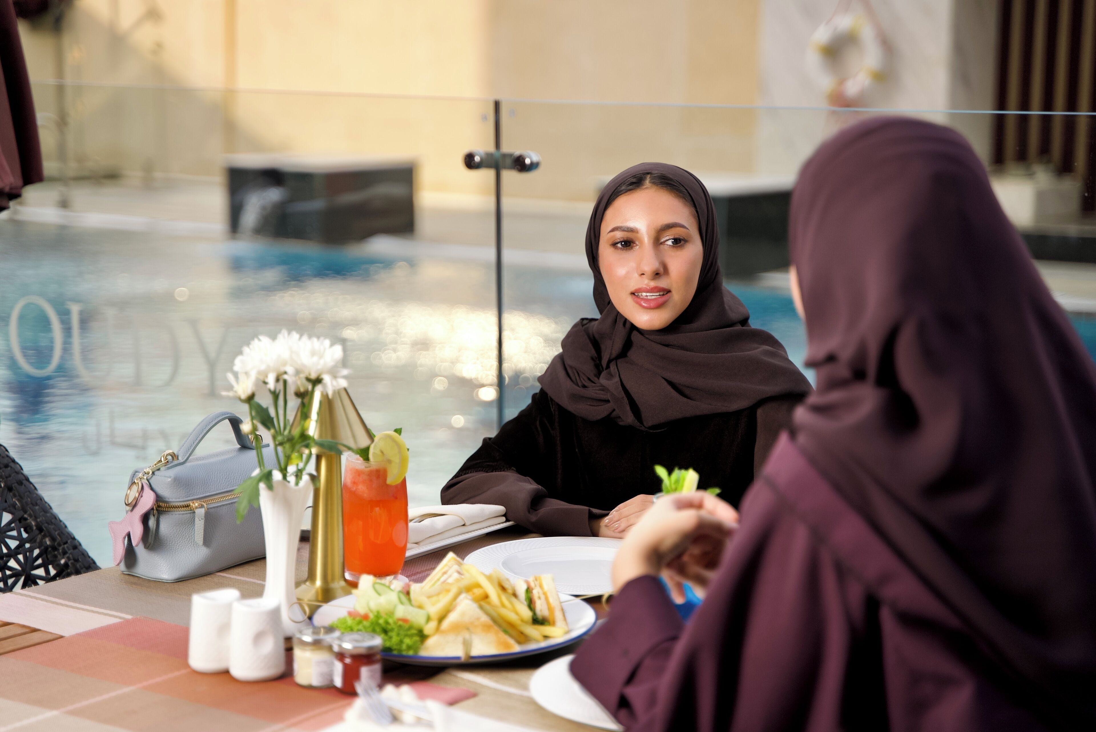 A dining table with a glass partition, a plate of food, a drink, and a handbag.