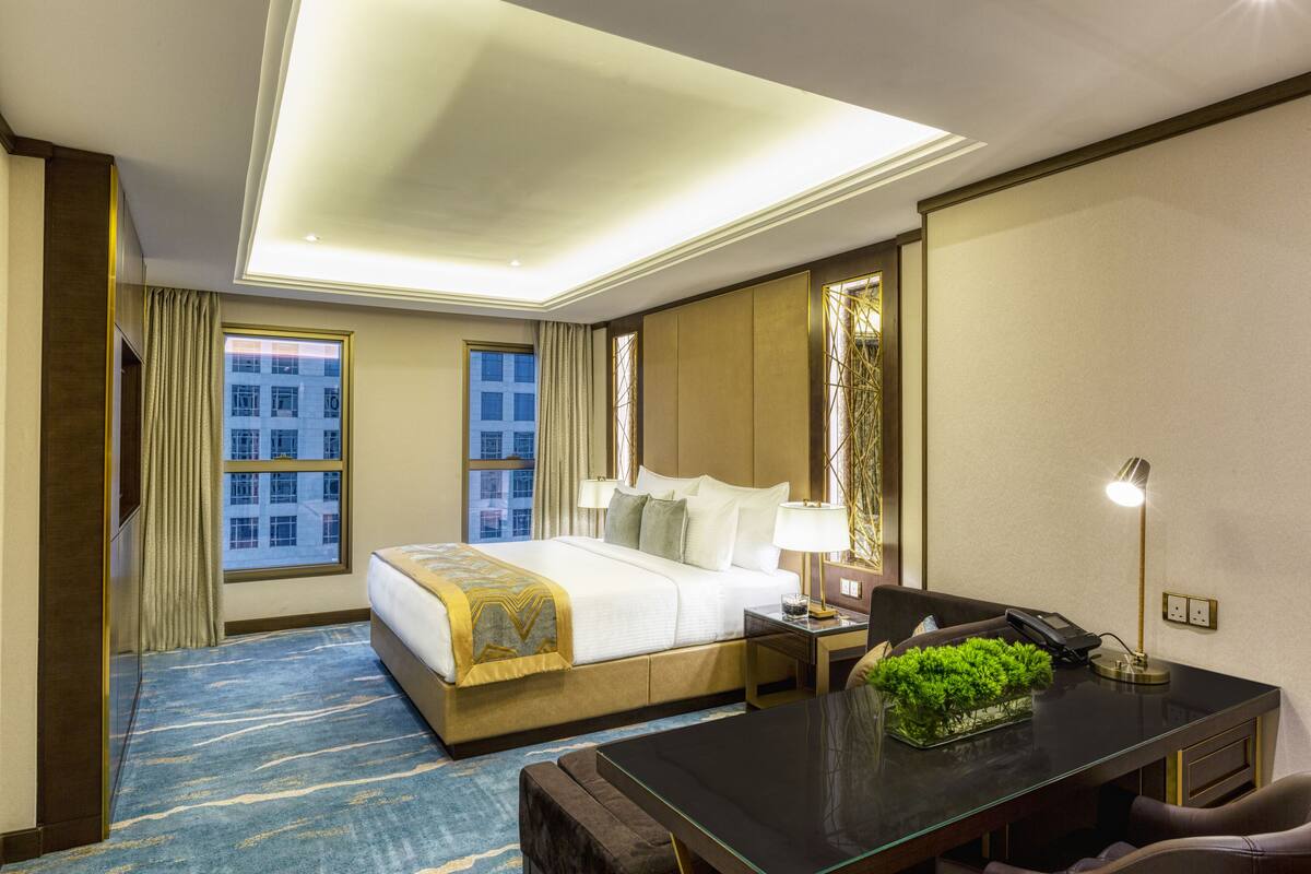 A hotel room with a large bed, a desk with a telephone, a lamp, and a small plant.