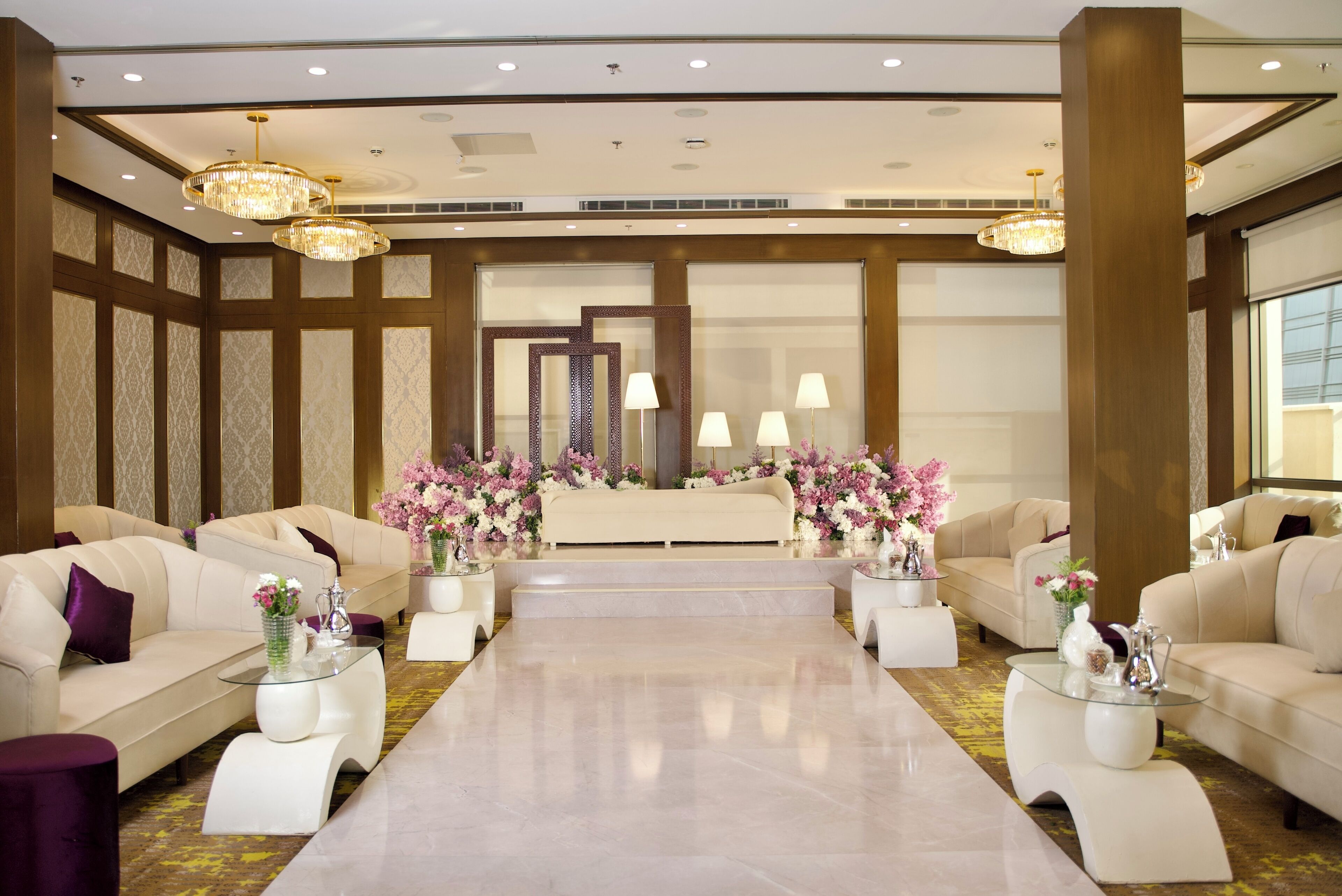 A spacious lobby with a central reception desk, flanked by sofas and armchairs, and adorned with floral arrangements.