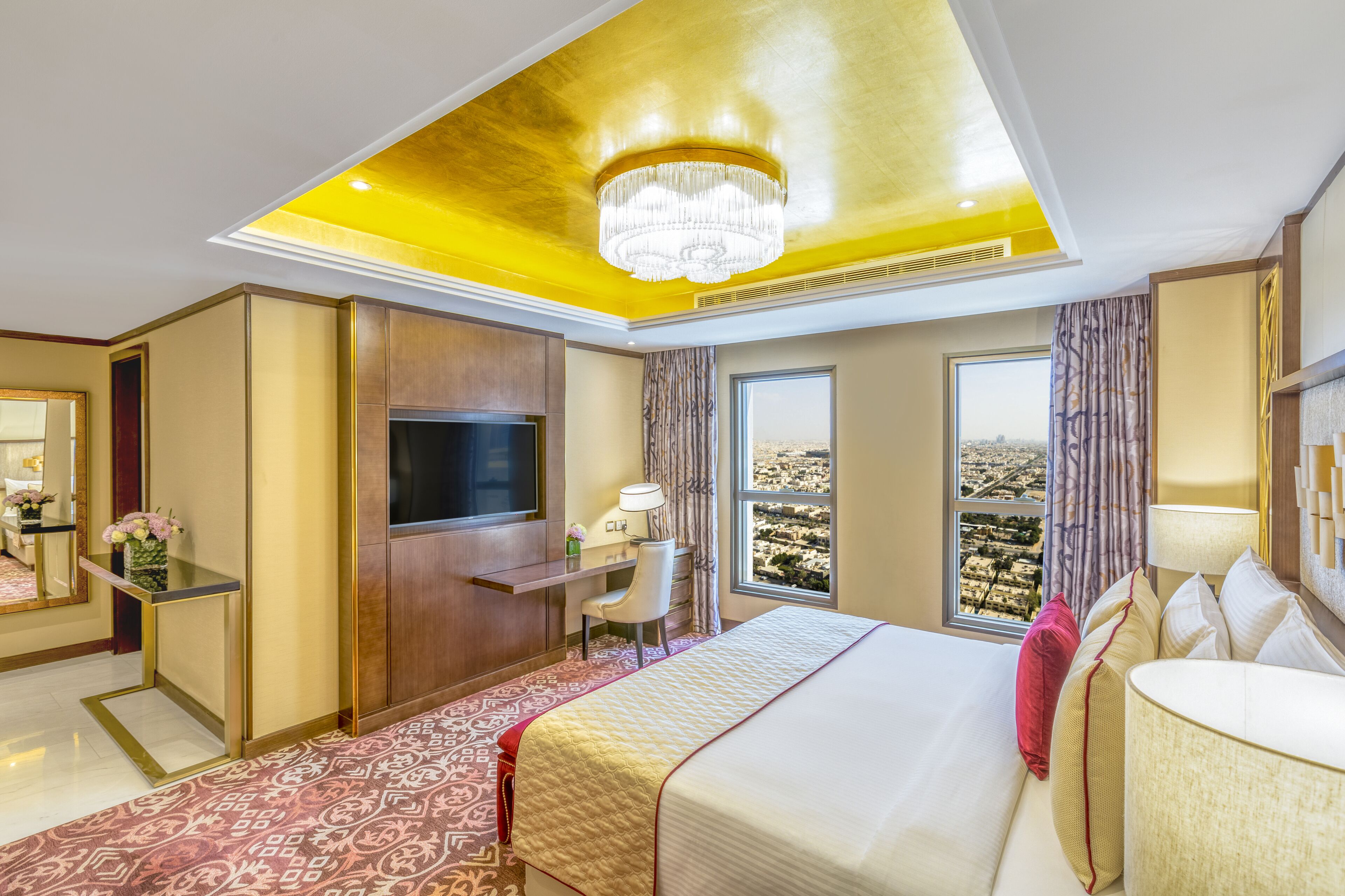 A hotel room with a large bed, a desk with a TV, a chair, and a view of the city.