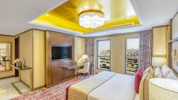 A hotel room with a large bed, a desk with a TV, a chair, and a view of the city.