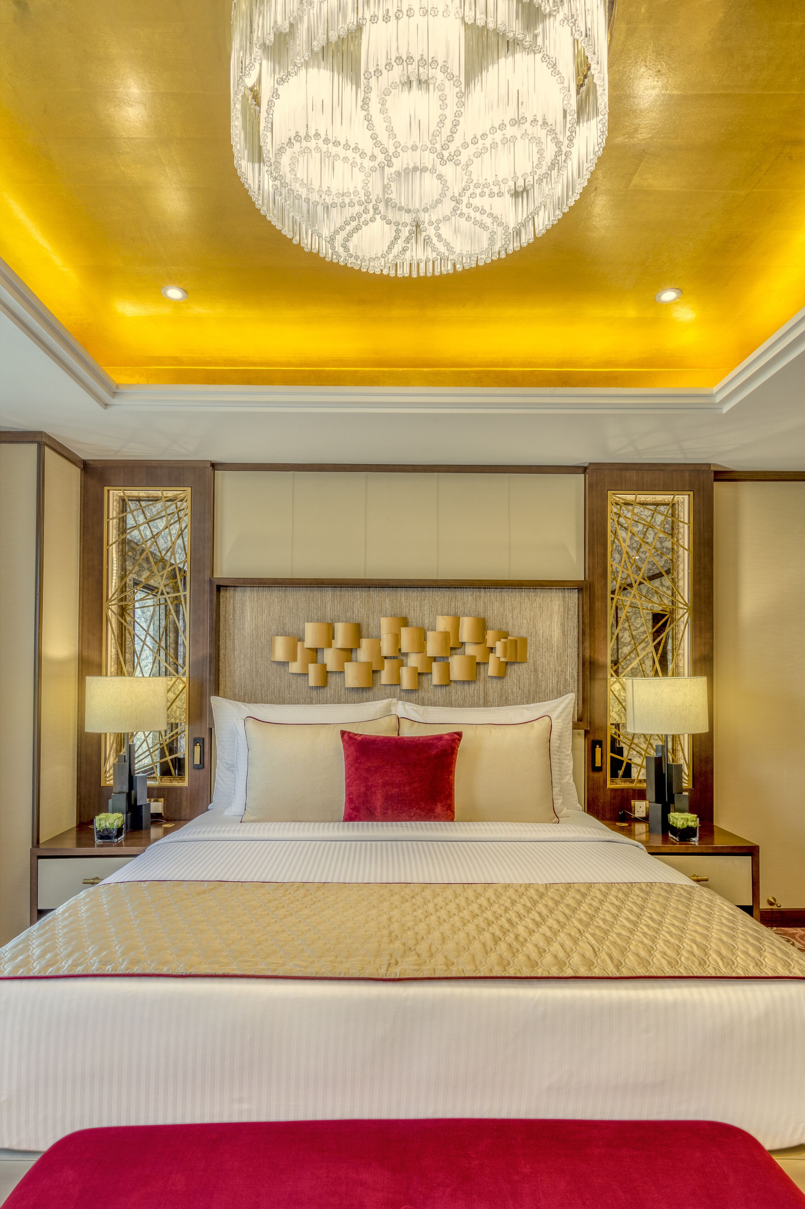 Een luxe hotelkamer met een groot bed, een kroonluchter en decoratieve wandpanelen.