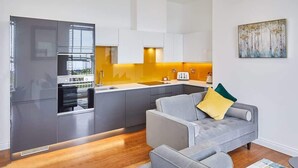 A modern kitchen with grey cabinets, a yellow backsplash, and a grey sofa with a yellow pillow. - Host & Stay | The Connell (Whitby)