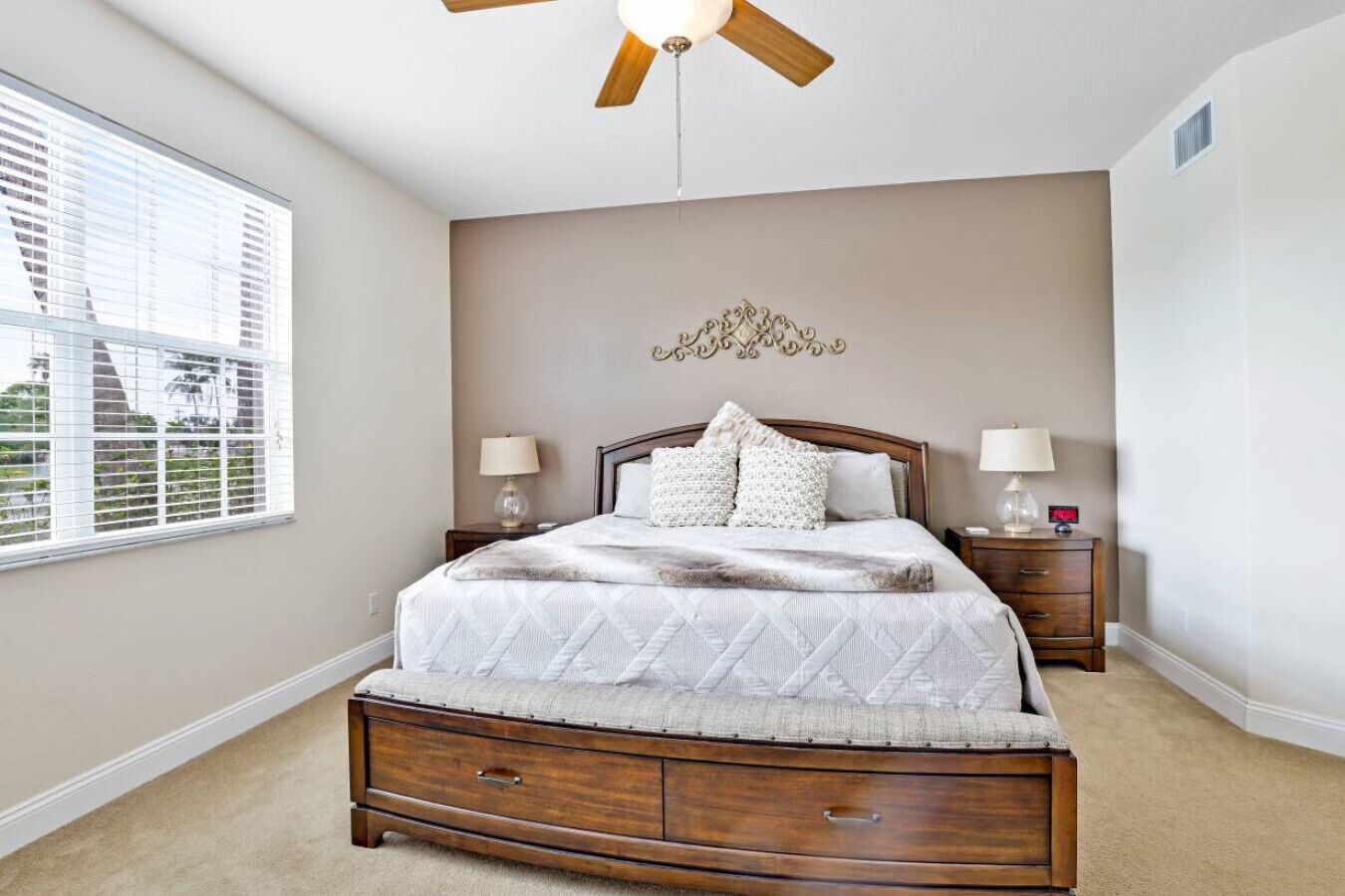 A bedroom with a bed, two bedside tables, a ceiling fan, and a window with blinds.