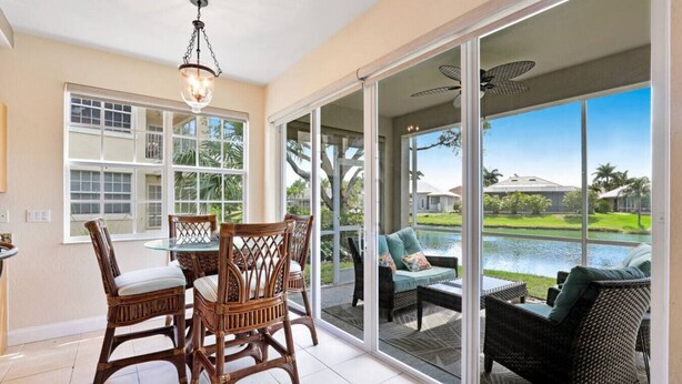A spacious room with a dining table and chairs, a large sliding glass door leading to an outdoor area with a view of a body of water and greenery. - Casa Boho | Cape Harbour 3/2 Coach Home (Cape Coral)