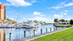 A marina with boats docked, a wooden walkway, and buildings in the background. - Casa Boho | Cape Harbour 3/2 Coach Home (Cape Coral)