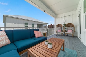 Un balcon abrité avec un canapé bleu, des fauteuils en osier et une table en bois.