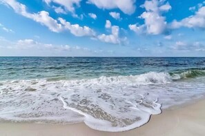 A beach with waves gently lapping onto the shore under a clear sky. - Heated Pool | Tiki Bar| Arcade, Fun games |3min to Beach| New Modern| (Gulf Shores)