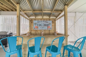 Un bar de style tiki, avec une structure en bois, une enseigne et trois chaises bleues.