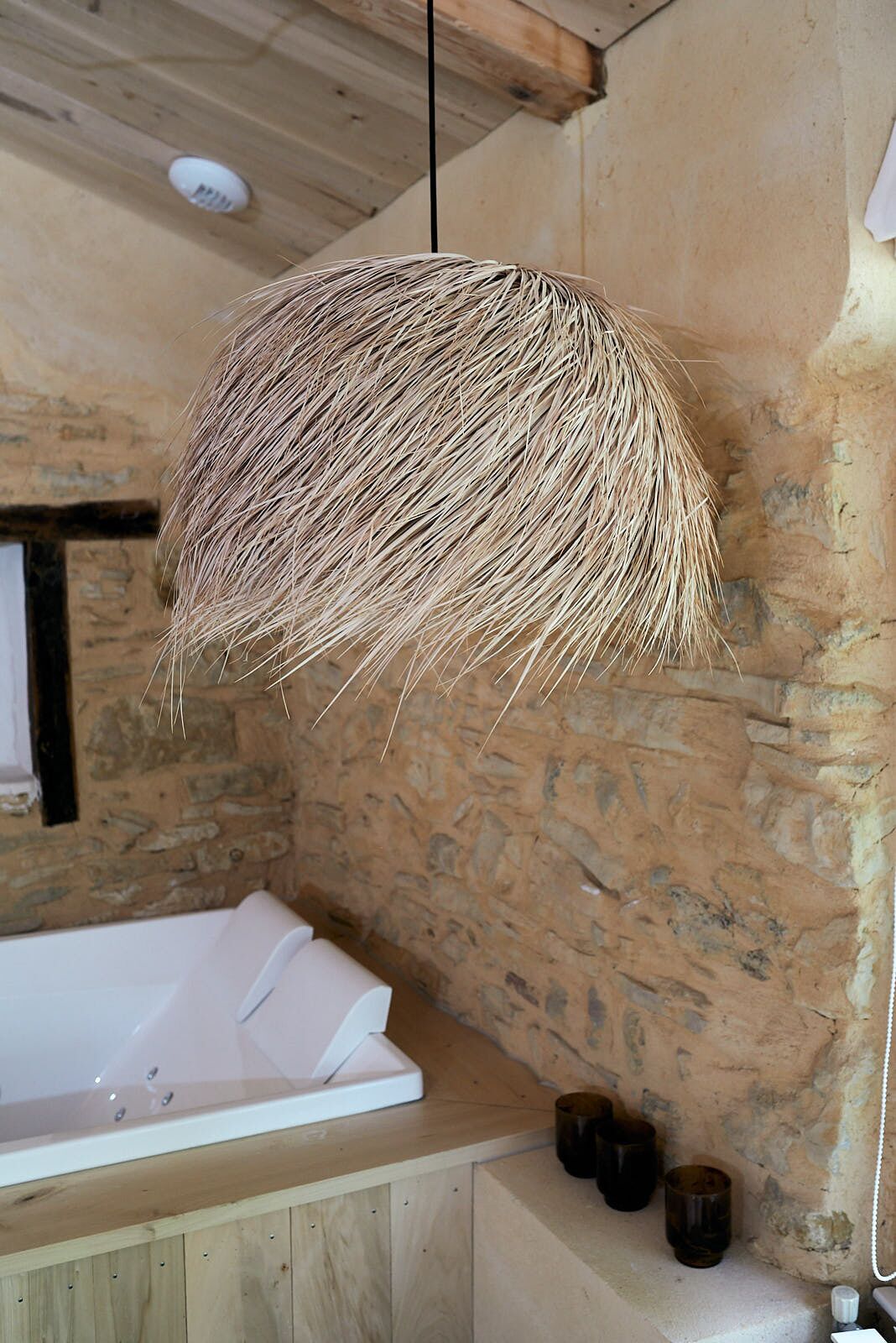 A rustic bathroom with a stone wall, a wooden ceiling, and a white bathtub.